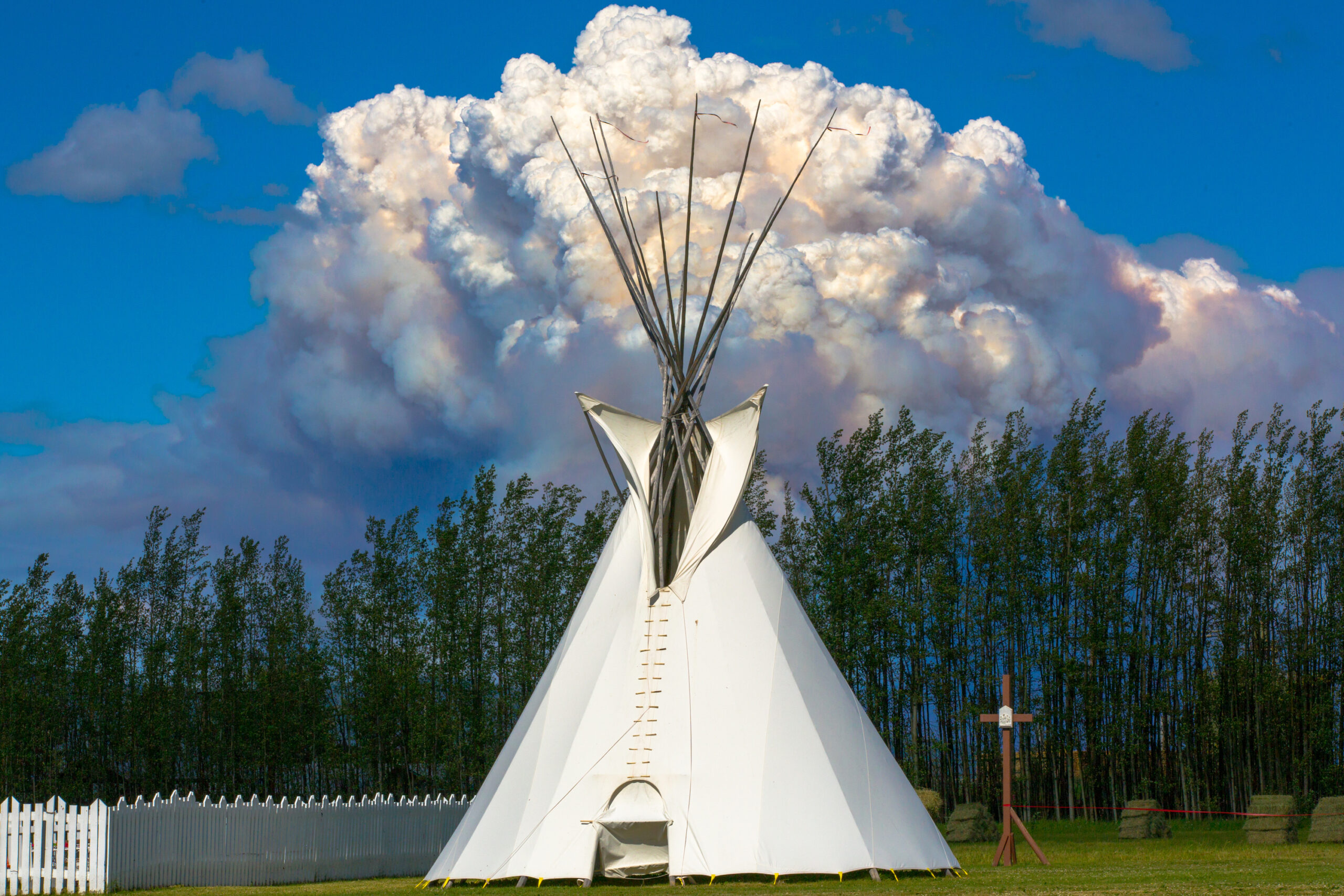 First Nations teepee with forest and wildfire smoke clouds in the background