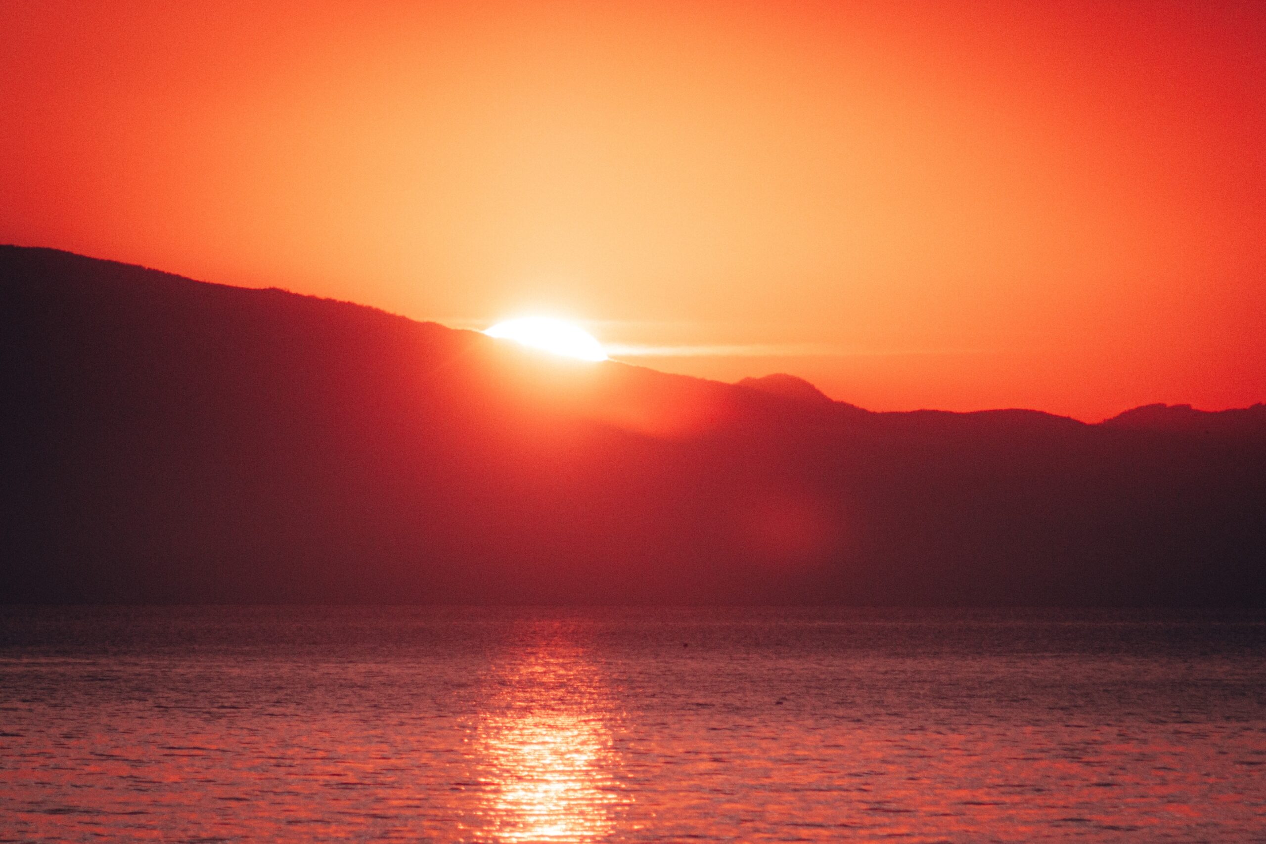 Lake in front of hills with glaring red sunset